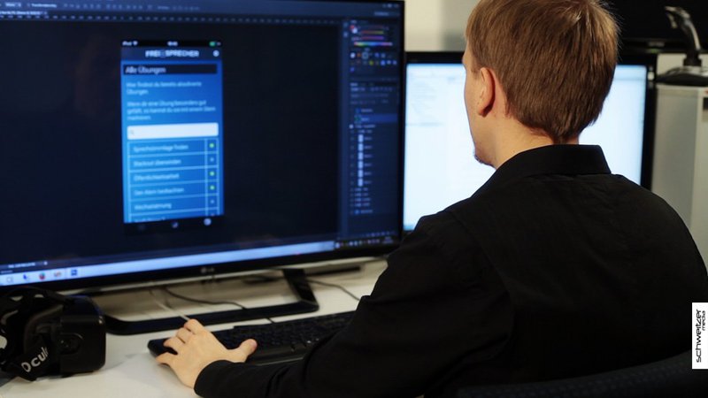 Ein Mann in schwarzem Pullover sitz vor einem Monitor und arbeitet an der Bedienoberfläche einer App.