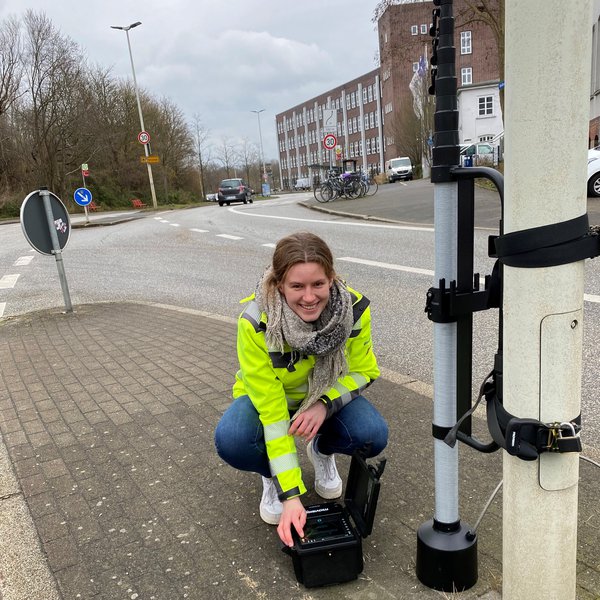 eine Studentin vom Studiengang Bauwesen hockt neben ihren Messgeräten am Verkehrsknotenpunkt Heikendorfer Weg in Kiel mit dem mobilen Verkehrsdatenerfassungssystem 