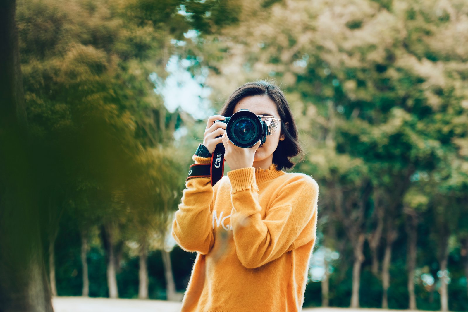 Eine Frau in orangenem Pullover hält eine Kamera um etwas zu fotografieren.