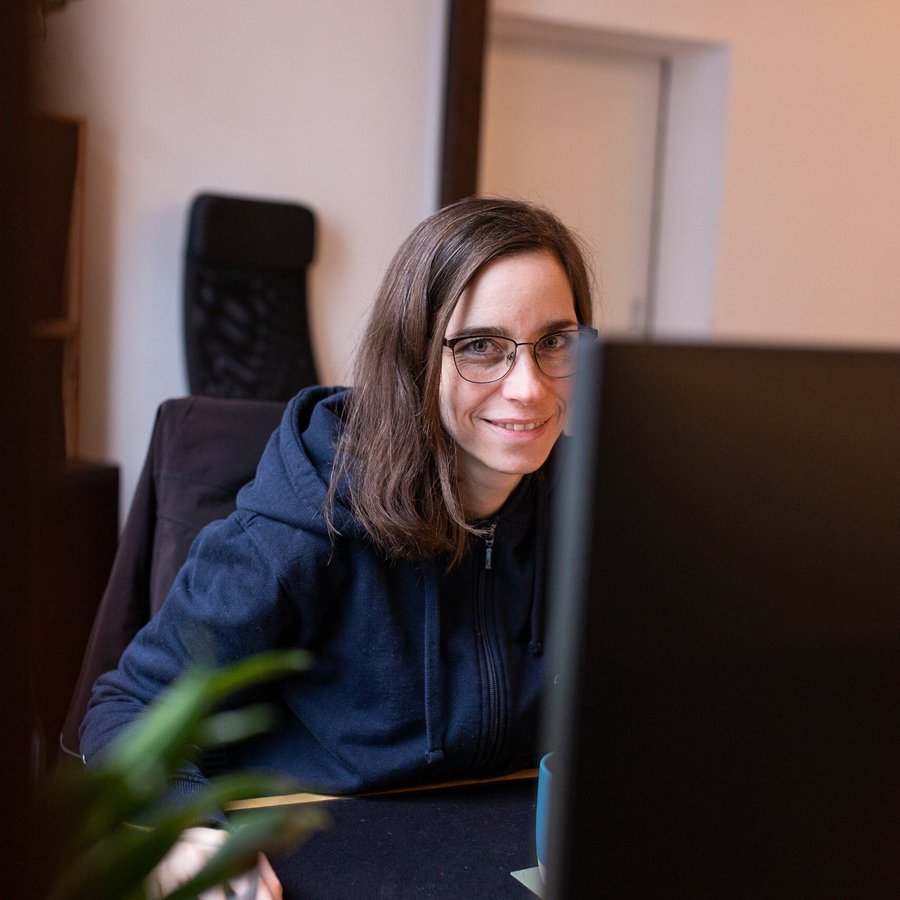 Eine Frau schaut lächelnd an einem Computerbildschirm vorbei in die Kamera