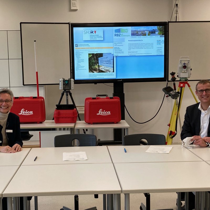 Martina Propf, Schulleiterin RBZ am Schützenpark und Prof. Dr. Björn Christensen, Präsident der FH Kiel, sitzen an einem TIsch mit Abstand und lächeln in die Kamera.