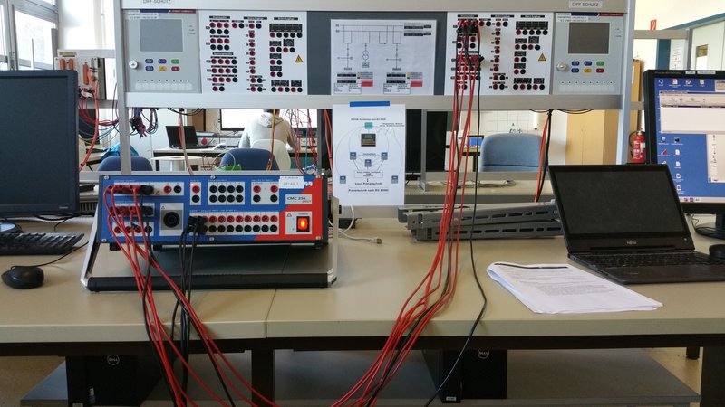 A picture showing a desk within a laboratory. On the Desk there is a physical circuit built up which is connected by red wires.