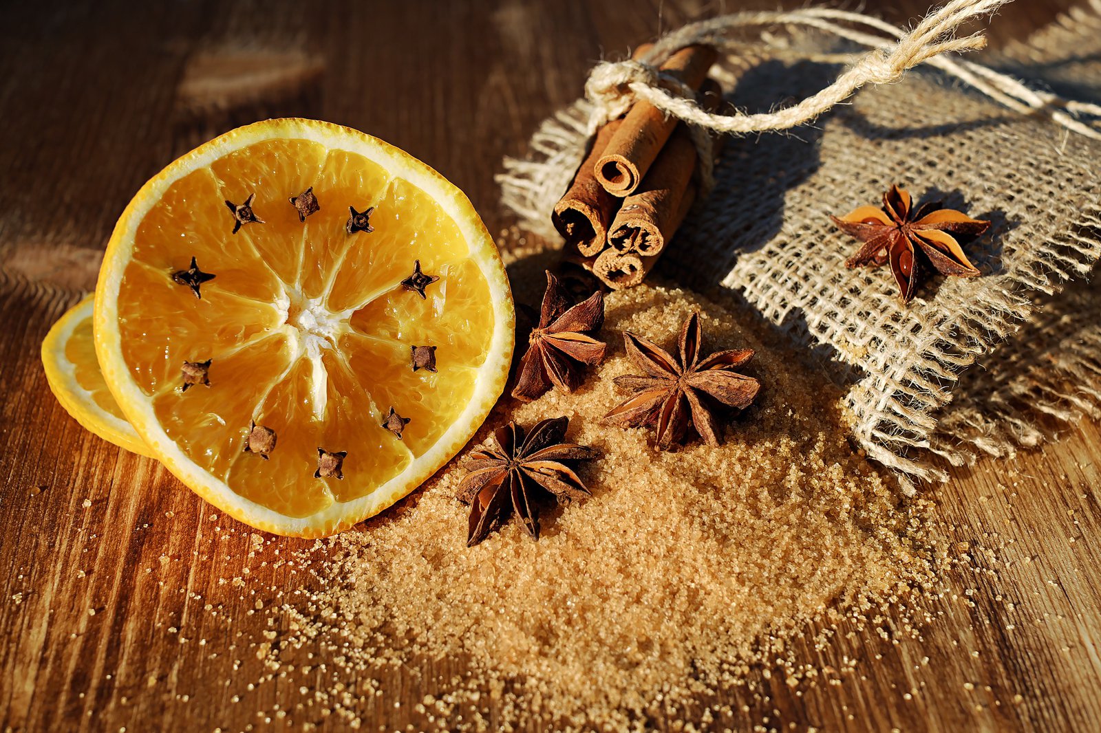 Ein Bund Zimtstangen, eine Orangenscheibe und Nelken umgeben einen Haufen braunen Zucker.