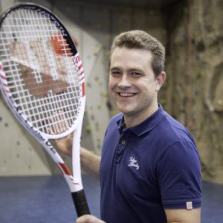 Ein Mann steht mit Tennisschläger in einer Boulder-Halle.