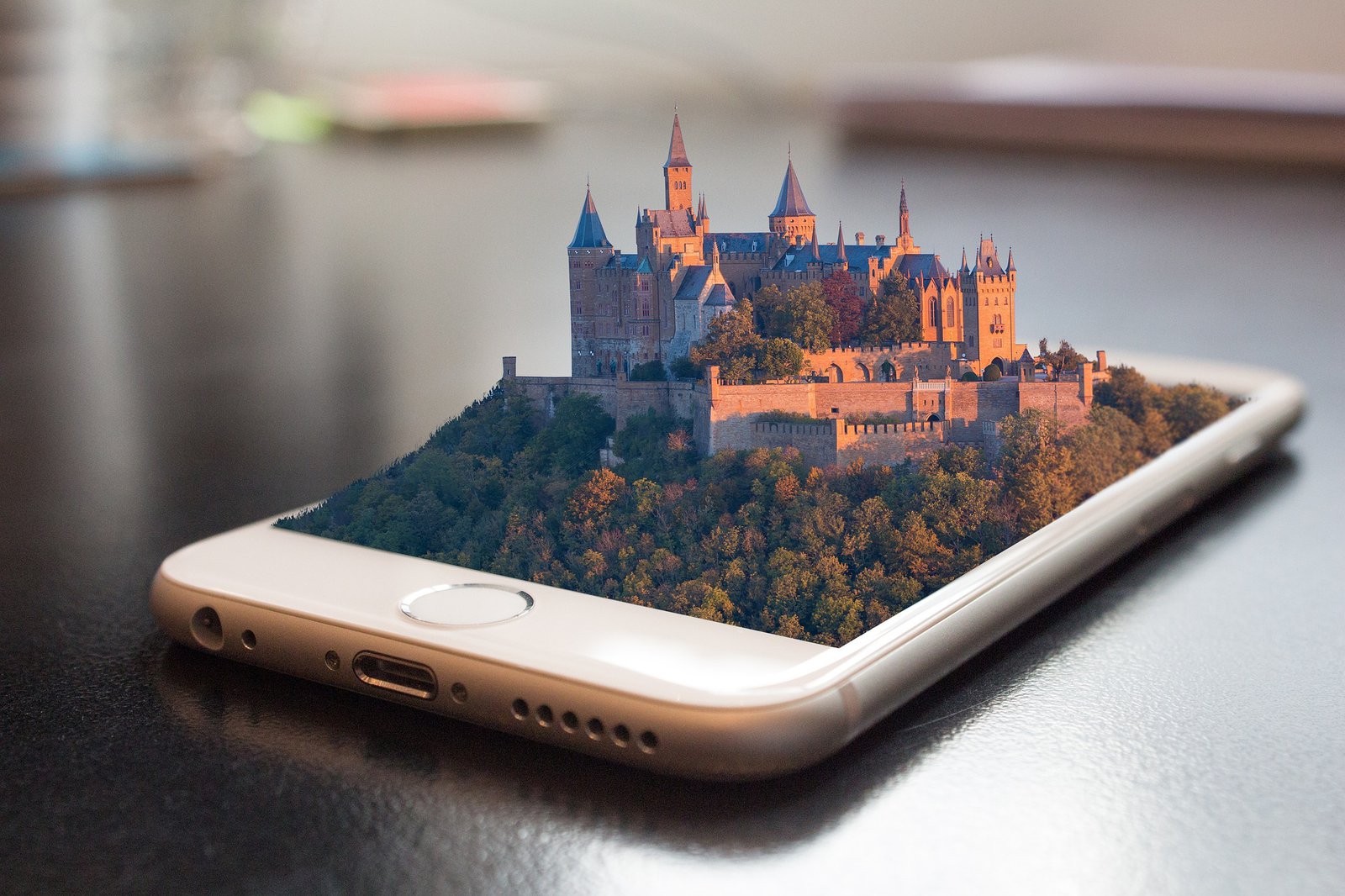 Ein Smartphone aus dem sich eine alte Burg mit umgebendem Wald erhebt.