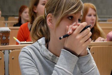 eine Studentin sitzt mit Stift in der Hand im Hörsaal