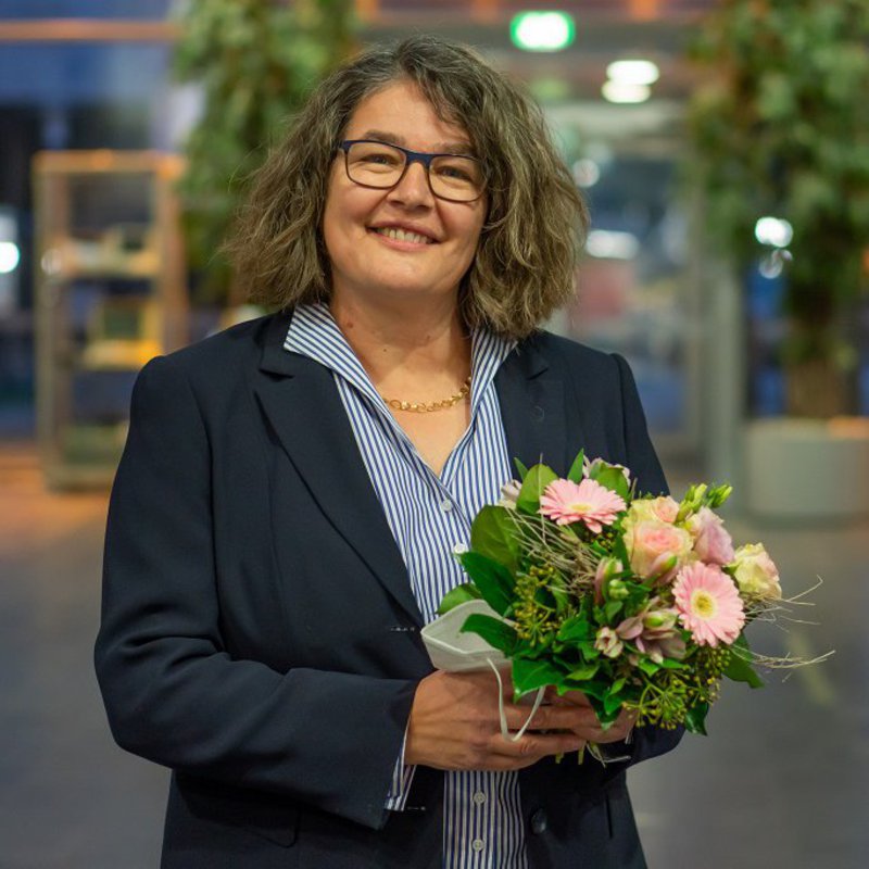  Ein Foto für Ihre Berichterstattung können Sie hier herunterladen.  Professorin Dr. Ruth Boerckel, die Dekanin des Fachbereichs Wirtschaft und künftige Vizepräsidentin der FH Kiel steht im Foyer des Mehrzwecksgebäudes und hält einen Blumenstrauß in Händen.