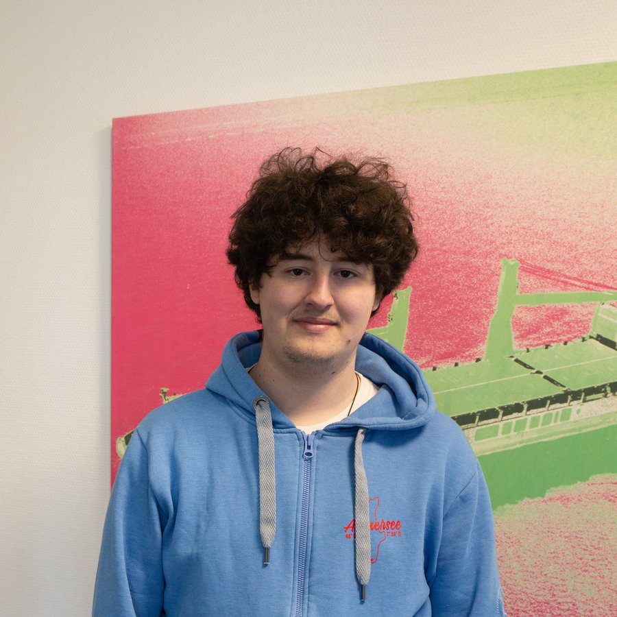 Schiffbaustudent Justus Schiszler an der FH Kiel vor einem Bild, auf dem ein Schiff angedeutet ist