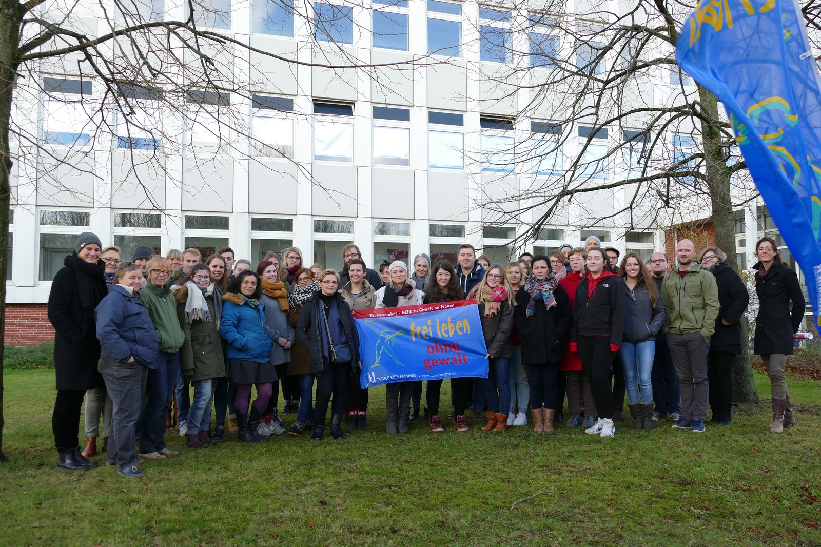 Eine GRuppe Studierender posiert vor einem weissen Gebäude und präsentiert ein Plakat.