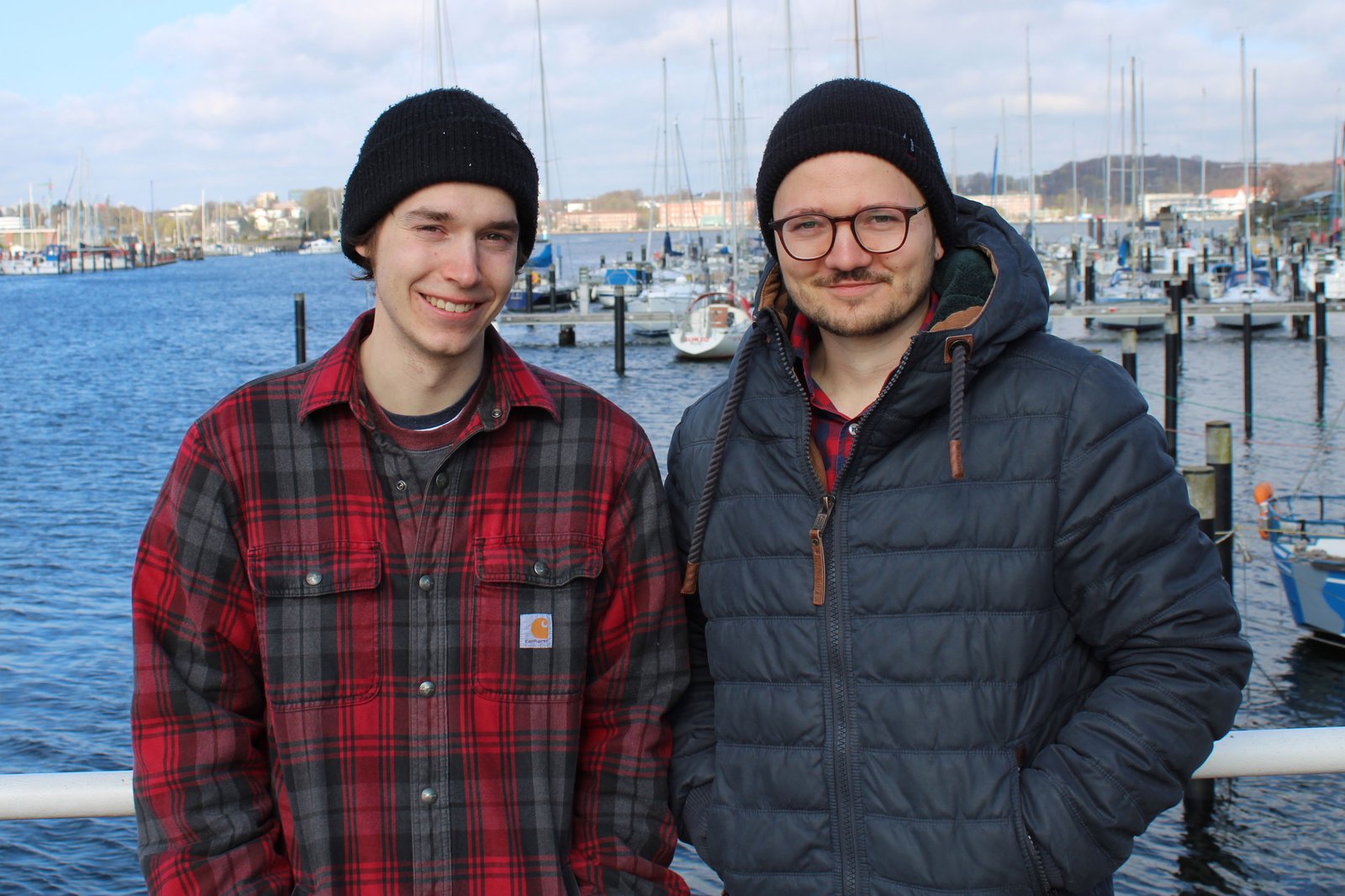 Zwei Männer mit Mütze posieren am Hafen der Schwentinemündung.