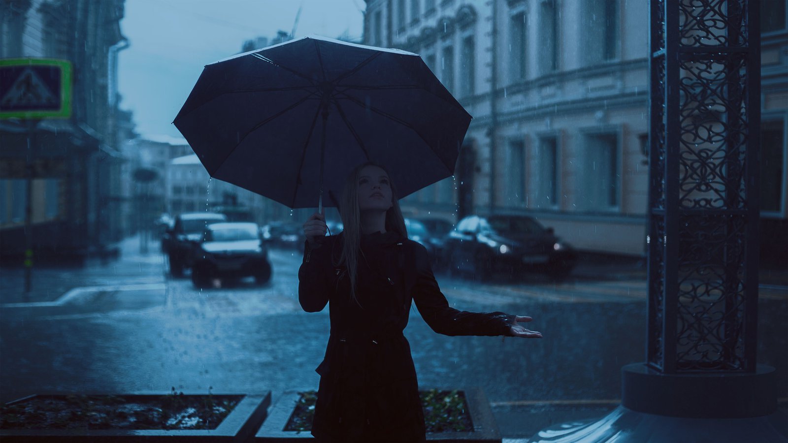 eine in Schwarz gekleidete Frau hält einen schwarzen Regenschrim und geht durch die Nacht.