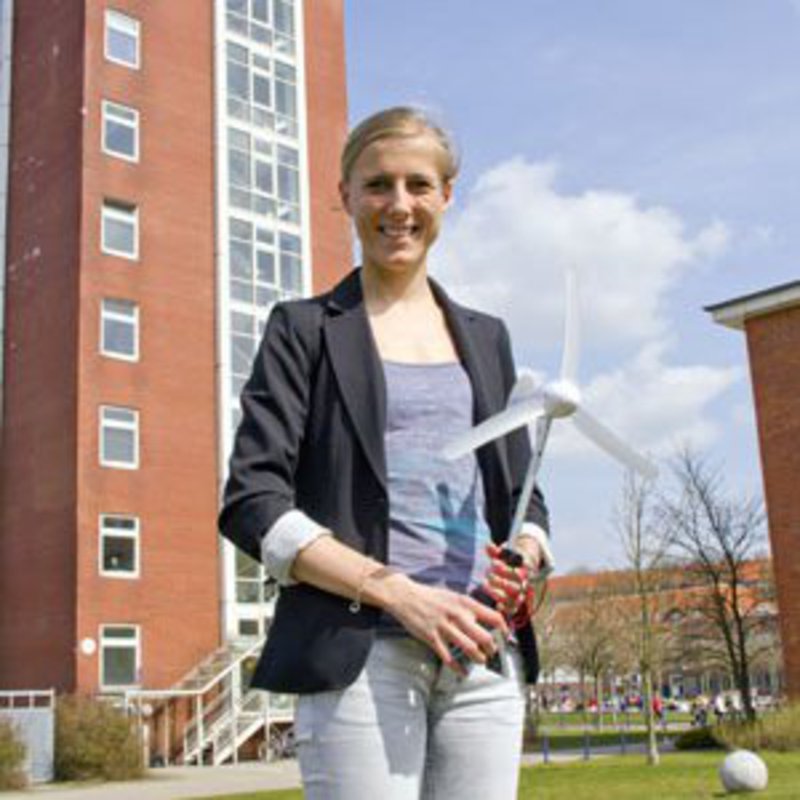 Eine Studentin posiert, mit einem Windrad in den Händen, auf dem Campus dr FH Kiel.