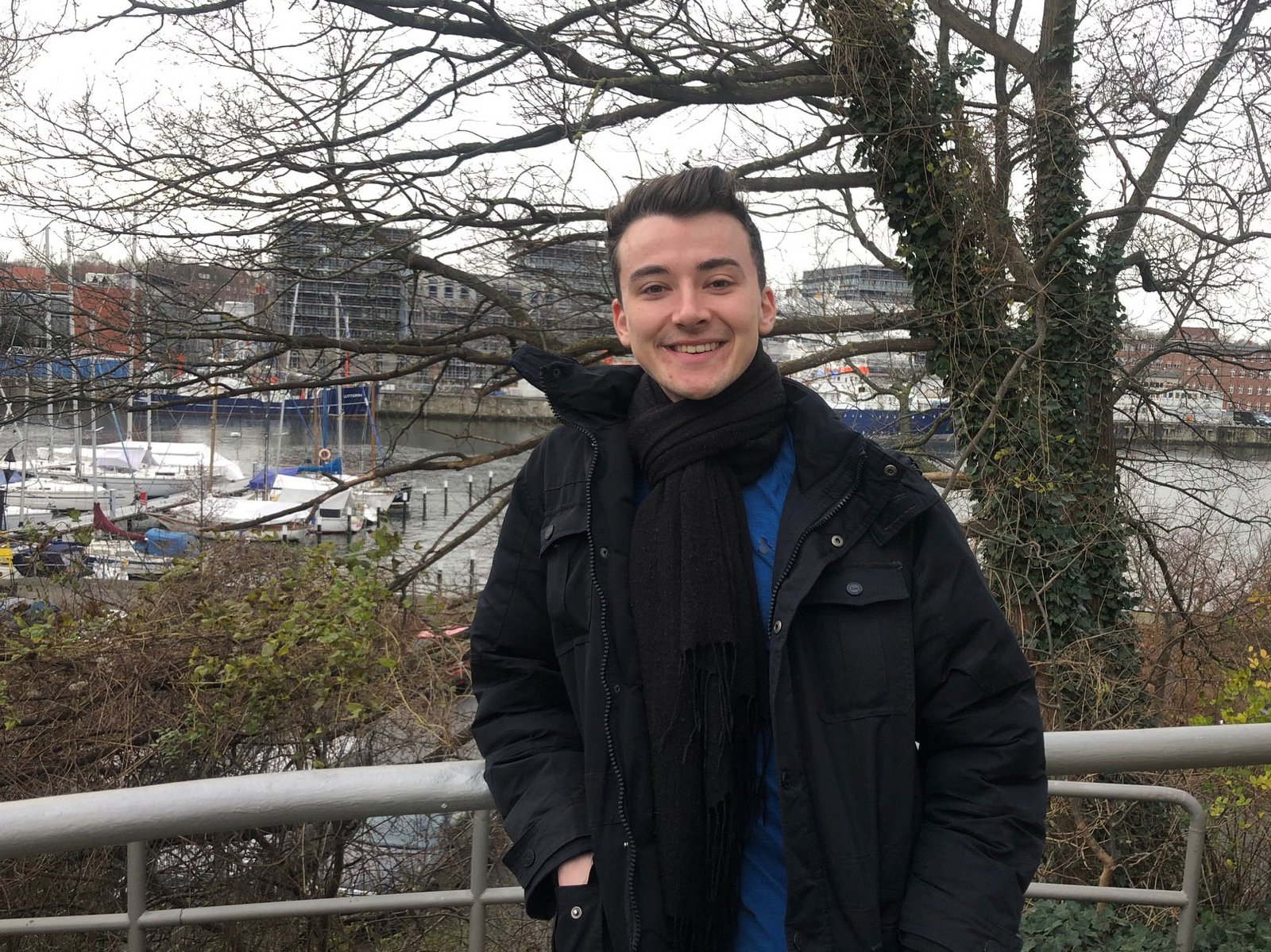 Ein Mann steht an ein Geländer angelehnt. Im Hintergrund ist der Hafen der Schwentine zu sehen.