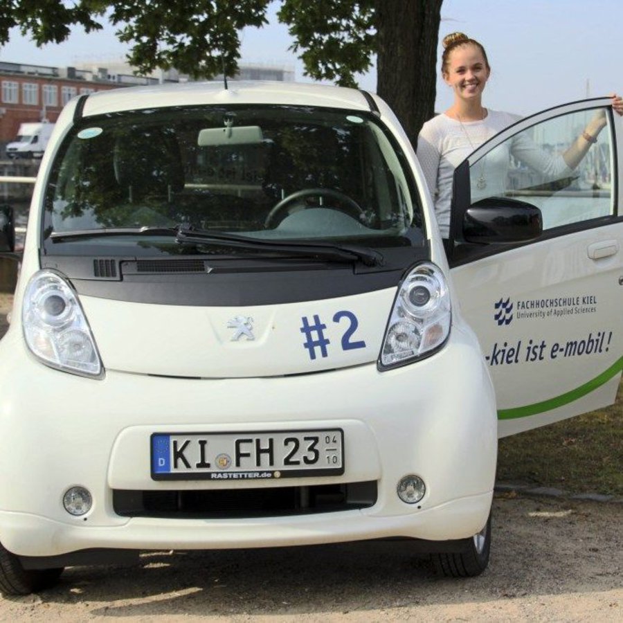 Eine Frau steht bei offener Tür neben einem Auto mit der Nummer Zwei.