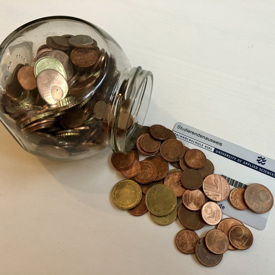 Eine umgekippte Spardose und Münzen, die auf einem Studierendenausweis liegen.