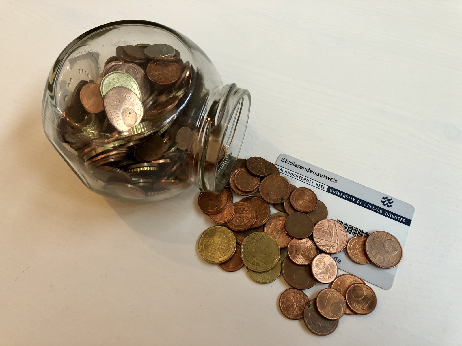 Eine umgekippte Spardose und Münzen, die auf einem Studierendenausweis liegen.