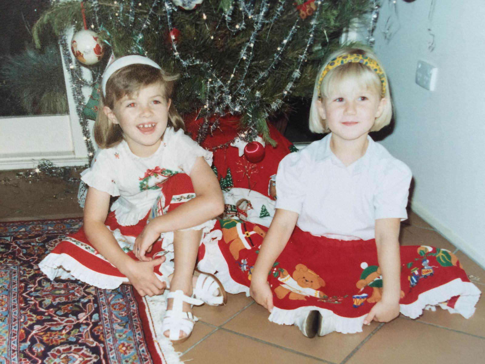Zwei junge Mädchen posieren in ihren Weihnachtsoutfits vor einem geschmückten Tannenbaum.