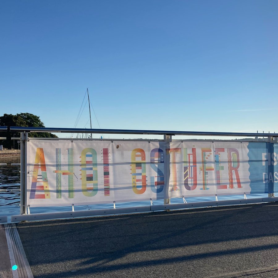 Banner an einem Geländer mit der Aufschrift: Ahoi Ostufer - Fisch, Forschung und Vergnügen, Das Fest auf dem Kieler Seefischmarkt, am 21. August 2022 