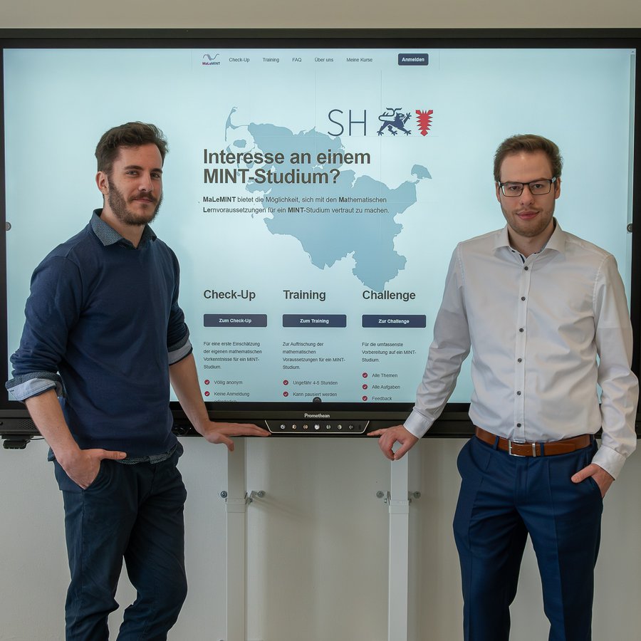 Zwei junge Männner, Jannik Brozy (links) und Jon Haase (rechts), stehen neben einer Leinwand, auf der die Startseite der Lernplattform MaLeMINT zu sehen ist. Foto: Matthias Riedel