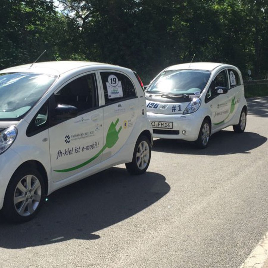 Zwei E-Autos stehen hintereinander an einer Ladesäule.