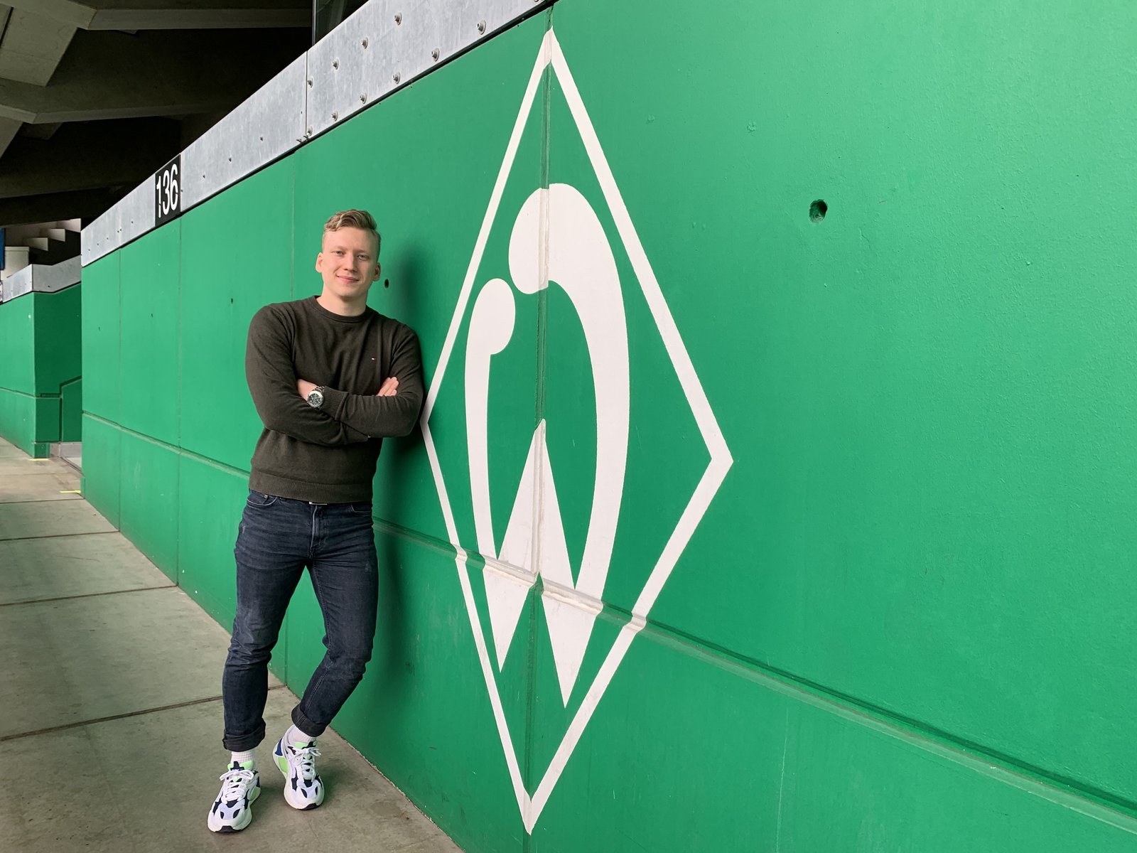 Lennard Worobic vor einer grünen Wand, auf der das Werder Bremen Logo zu sehen ist.