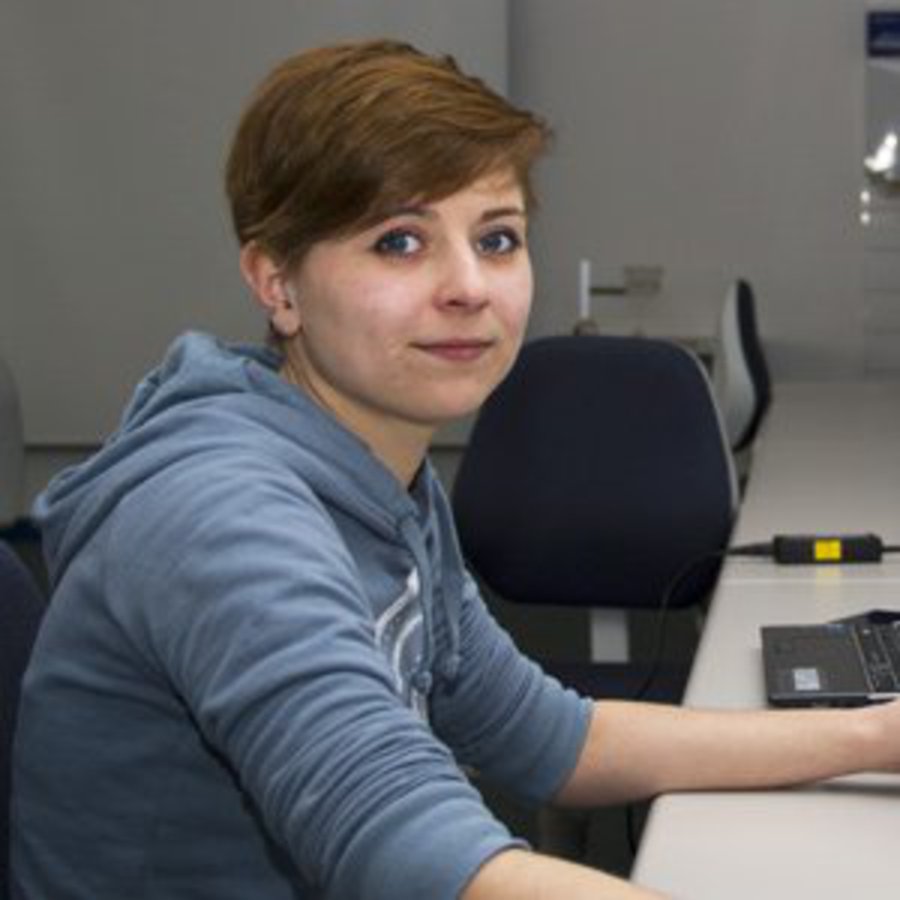Eine Frau mit kurzen Haaren, sitzt in einem Computerlabor.