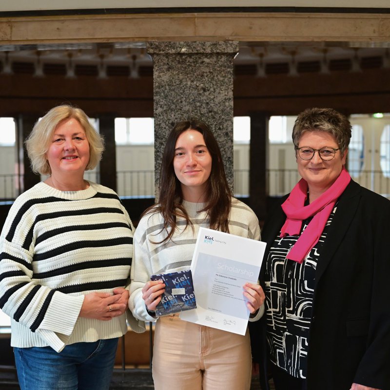 Das Foto zeigt drei Frauen im Foyer des Kieler Rathauses. (v.l.n.r. Stadtpräsidentin Bettina Aust, Stipendiatin Eléonore Chalkidis und Bürgermeisterin und Wissenschaftsdezernentin Renate Treutel). 