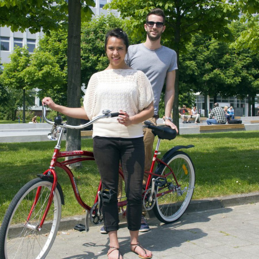 Ein Student und eine Studentin halten gemeinsam ein rotes Tandemrad.