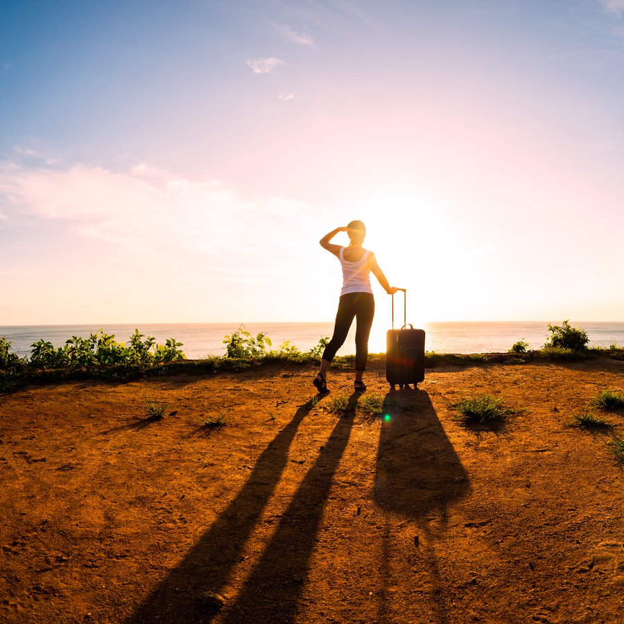 eine Frau mit Koffer blickt in den Sonnenuntergang