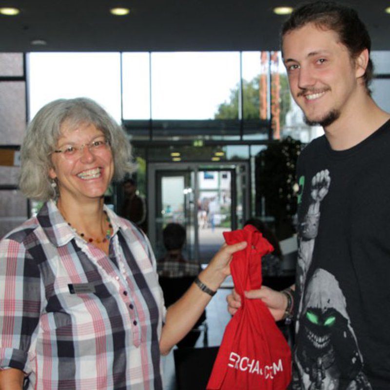 Geschäftsführerin Kirsten Bründel überreicht Ersti Linus Hasler einen roten Beutel zur Begrüßung