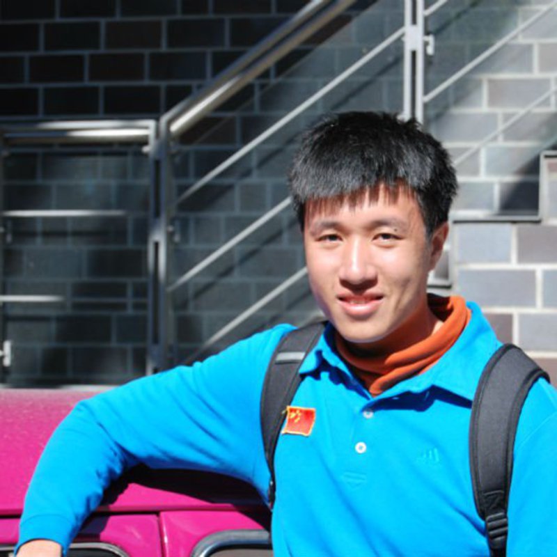 Ein Mann posiert im Freien für die Kamera. Auf seinem blauen Pullover ist eine chinesische Flagge zu erkennen.