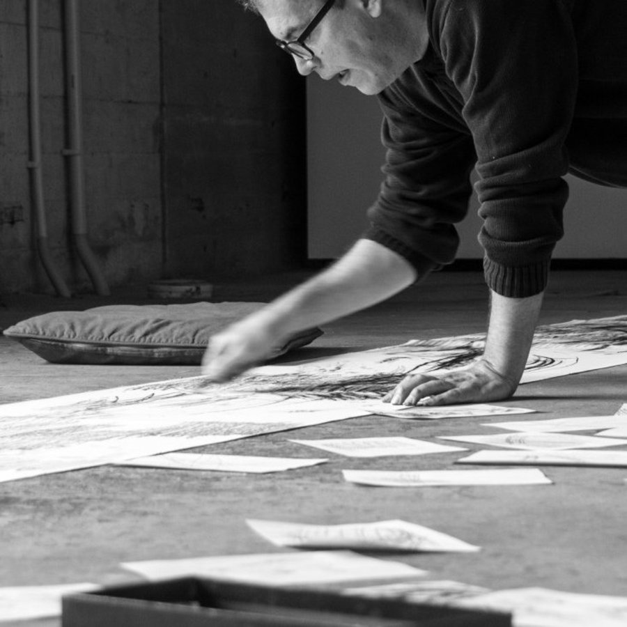 Das Schwarz-Weiß-Bild zeigt wie ein Mann seine Werke auf dem Boden bearbeitet.