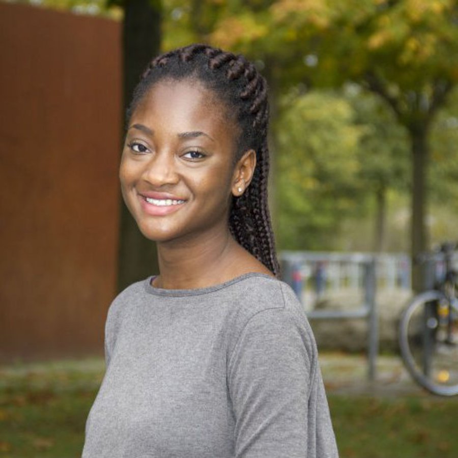 Eine Studentin mit geflochtenen Haaren lächelt freundlich in die Kamera.