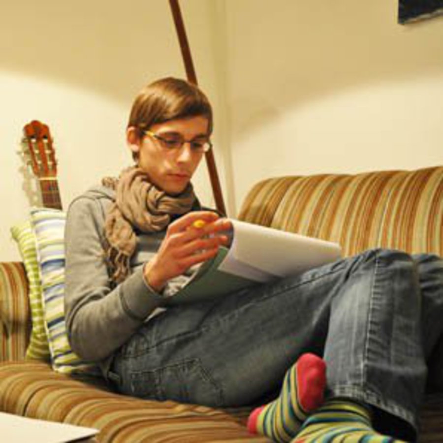 Ein Student sitzt lesend auf einem Sofa.