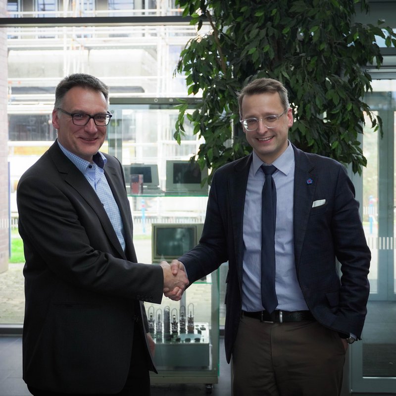 Prof. Claus Neumann steht links neben Prof. Dr. Tobias Hochscherf im Foyer des Audimax und gratuliert ihm. 