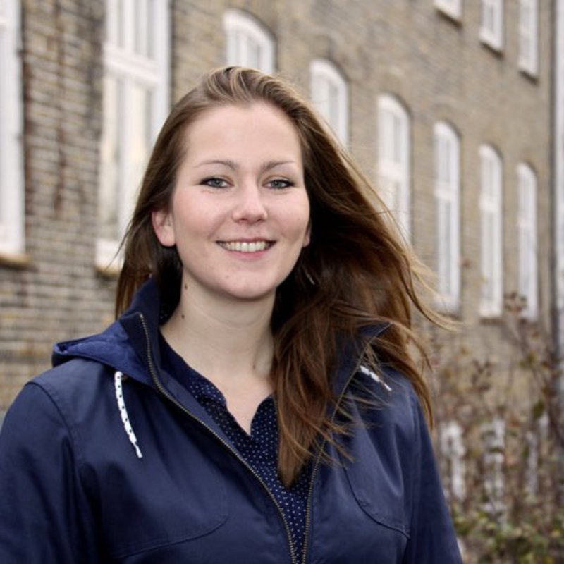 Eine Frau steht in ihrem blauen Pullover an einem Hörsaalgebäude, der FH Kiel.