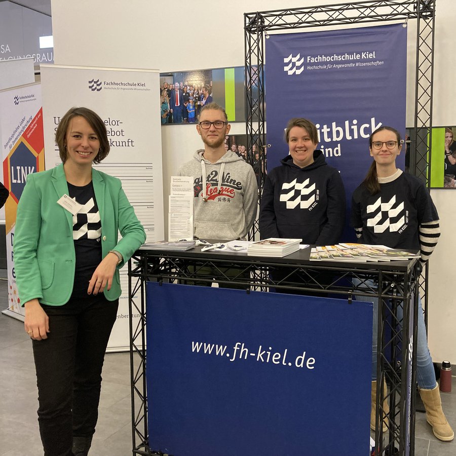 Drei Frauen und ein Mann stehen an einem Messestand und schauen lächelnd in die Kamera