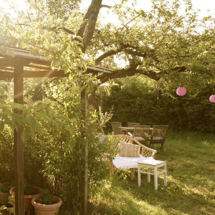 Ein schöner grüner Garten, mit einer gemütlichen Sitzecke und einem Balkendach.