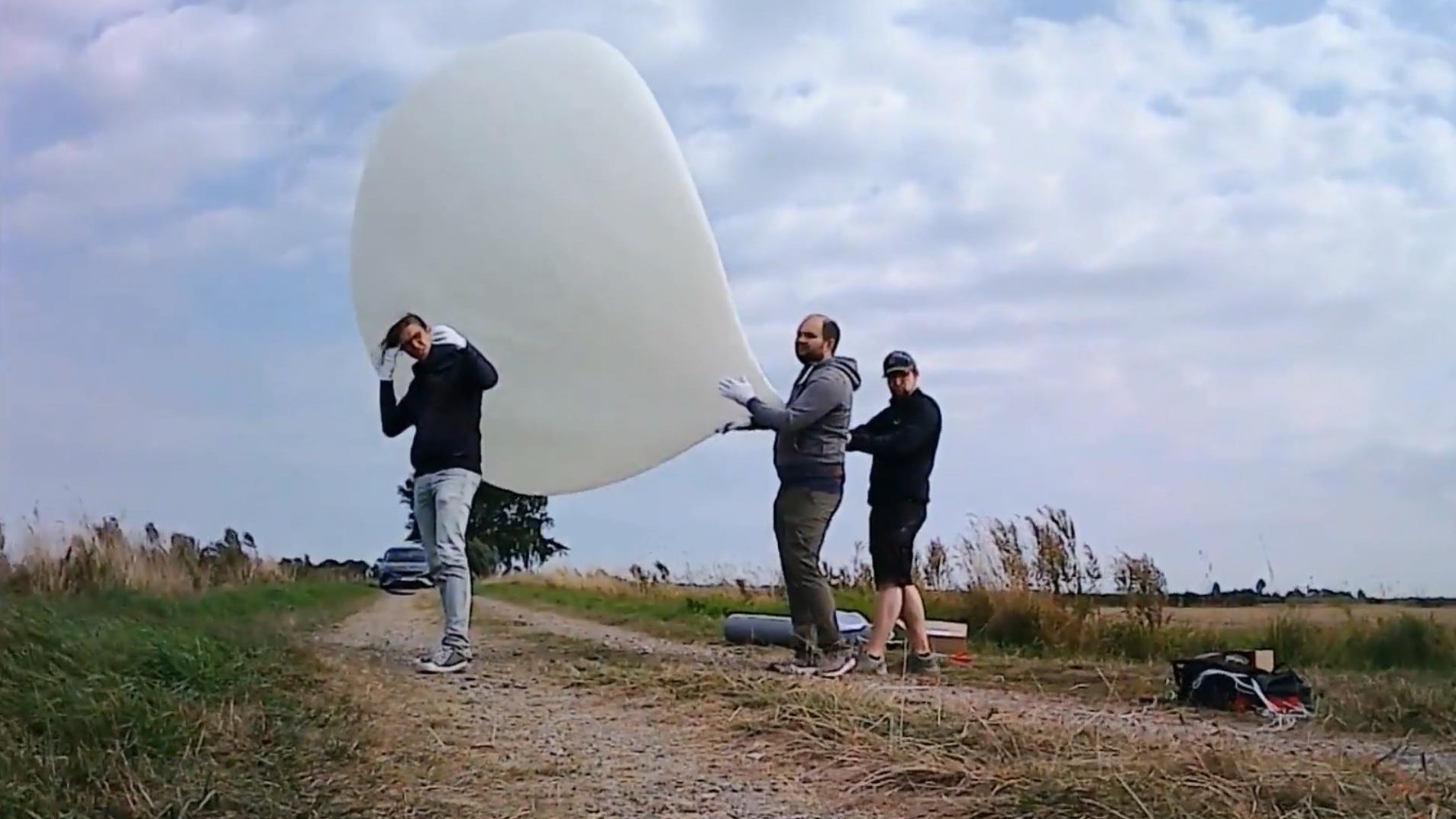 drei Menschen auf freiem Feld mit Wetterballon