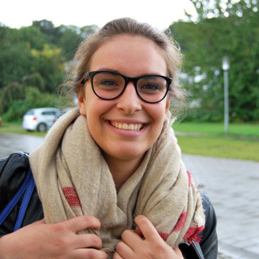 Eine Frau mit schwarzer Brille und Schal lächelt motiviert in die Kamera.