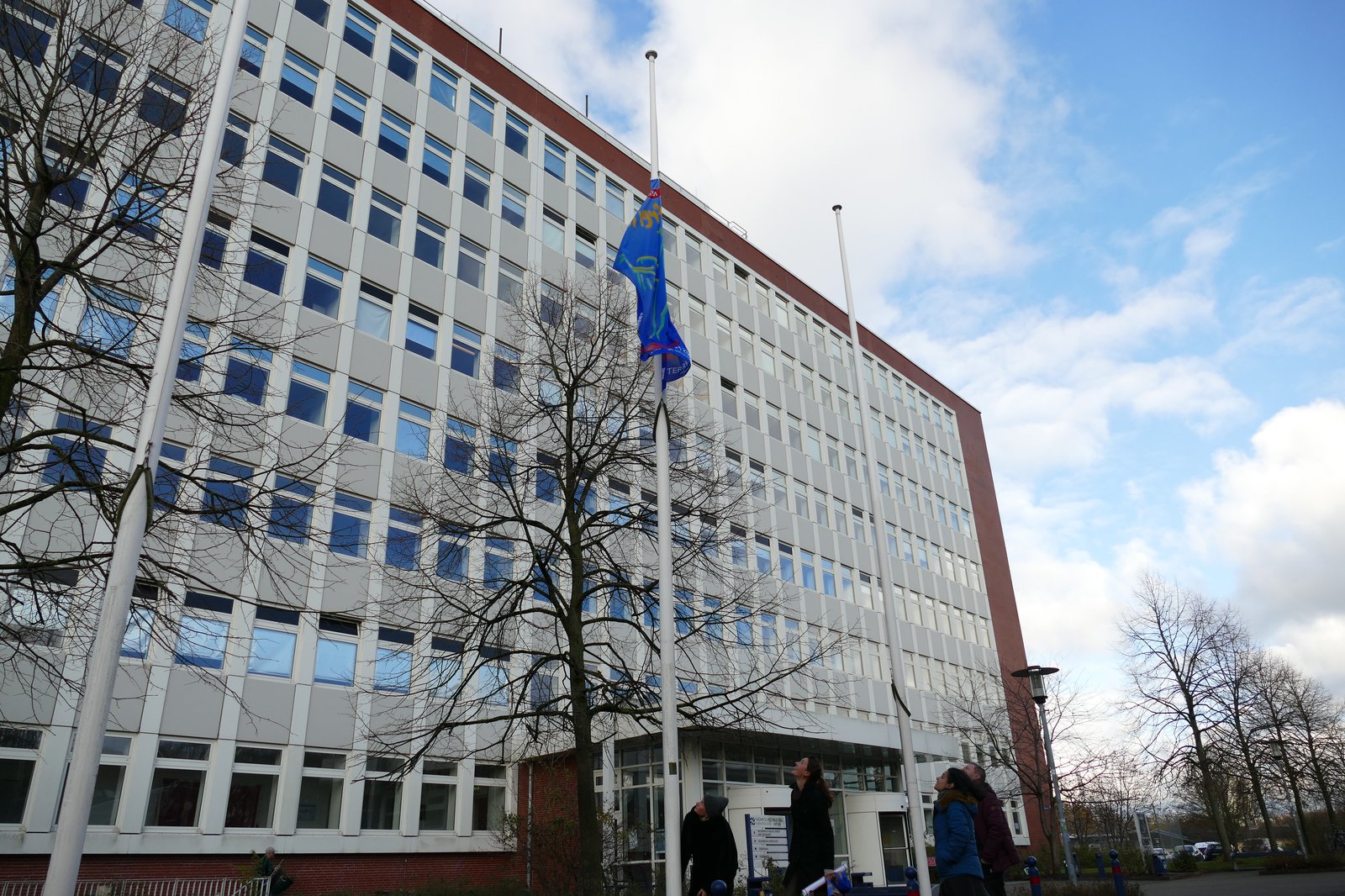 Eine auf Halbmast hängende blaue Fahne vor einem weissen Gebäude.