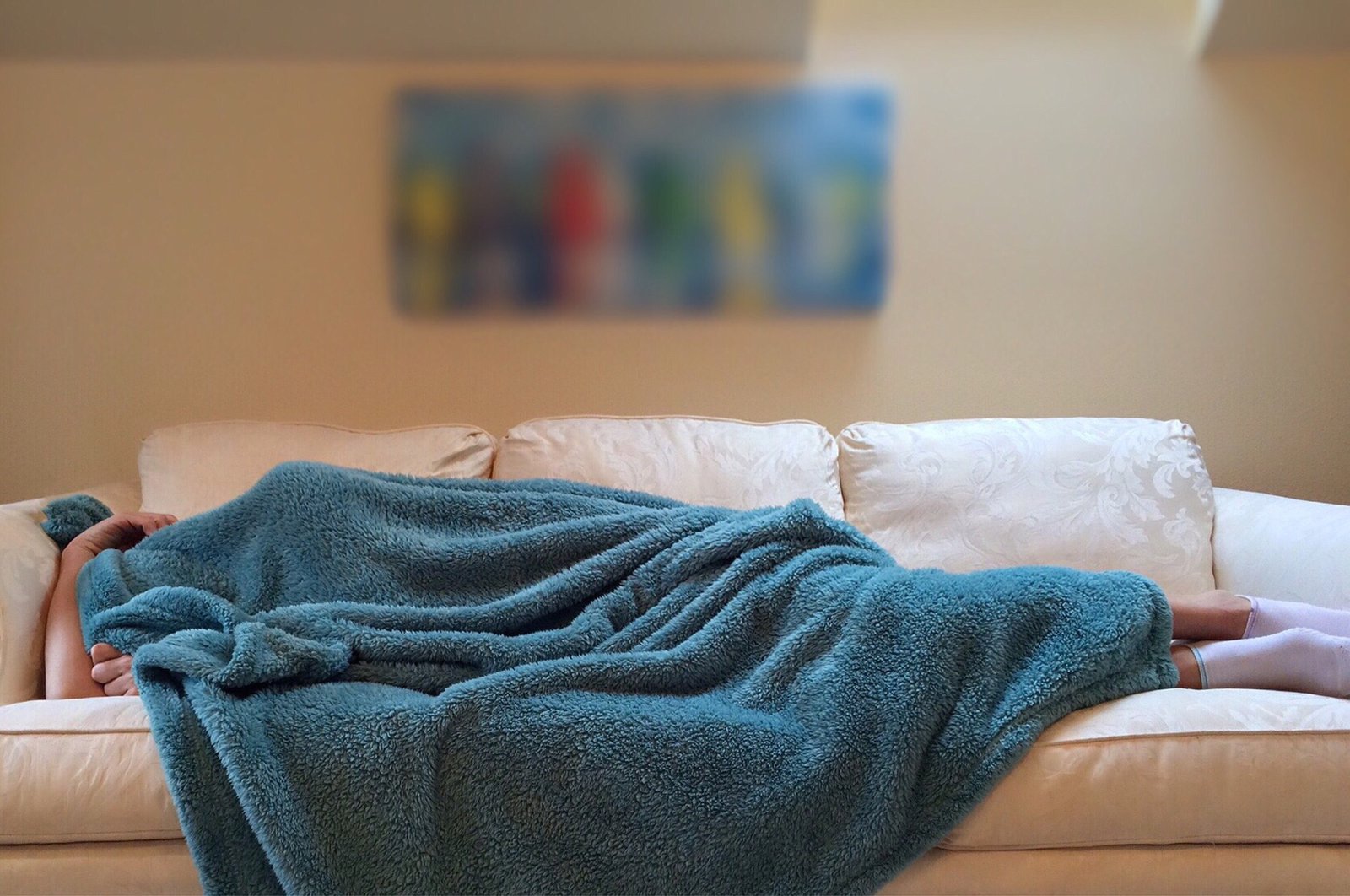 Eine auf einem Sofa liegende Person versteckt sich unter einer Wolldecke.