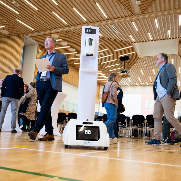 In einem Foyer stehen Menschen in der Mitte ein Roboter.