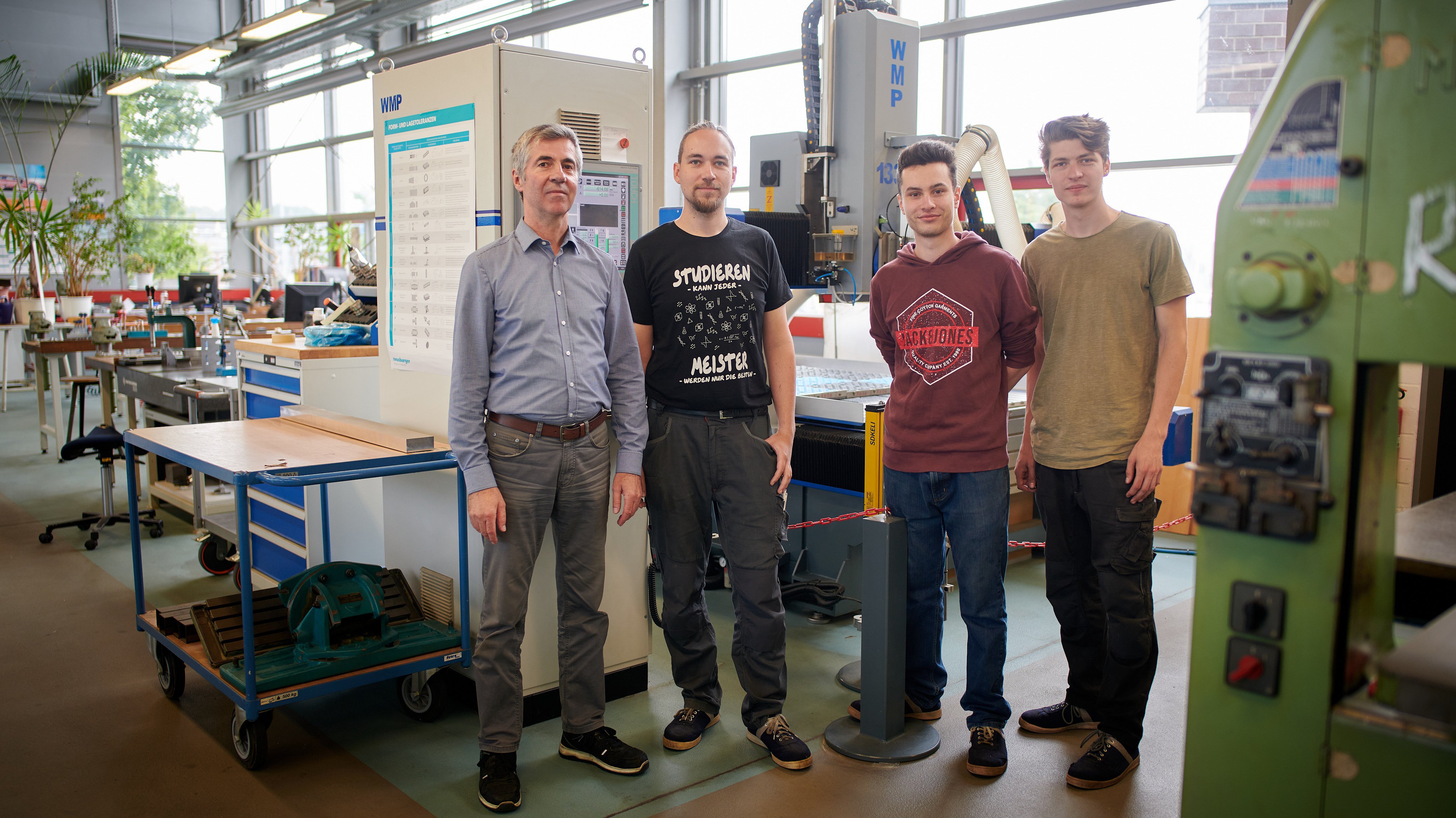 Vier Männer stehen in einer Werkstatt vor Maschinen und schauen lächelnd in die Kamera