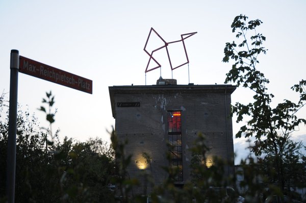 Ein Bunkergebäude tut sich hinter einer Hecke auf.