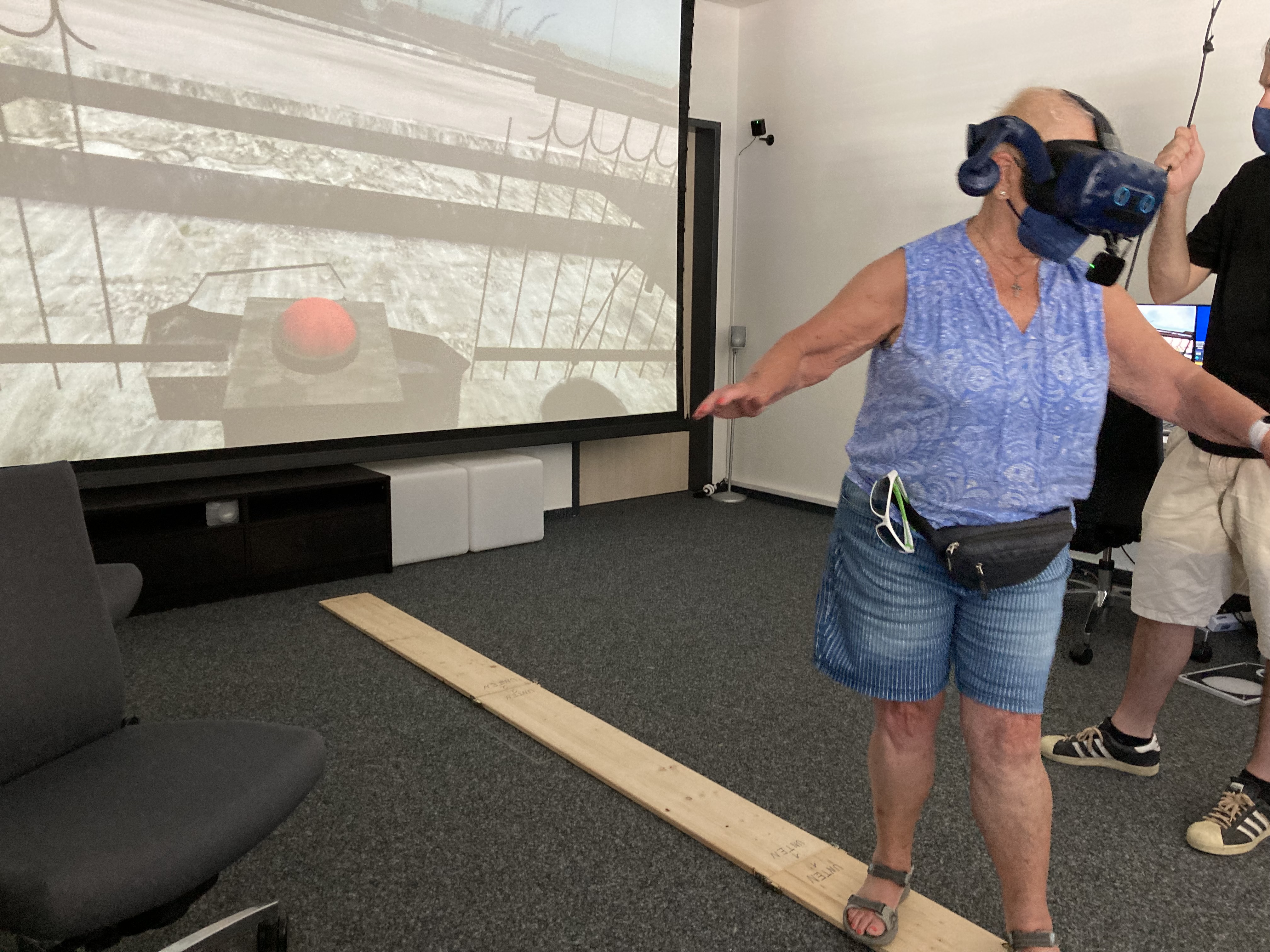 Eine Frau balanciert auf einer Holzplanke. Sie trägt eine VR-Brille.