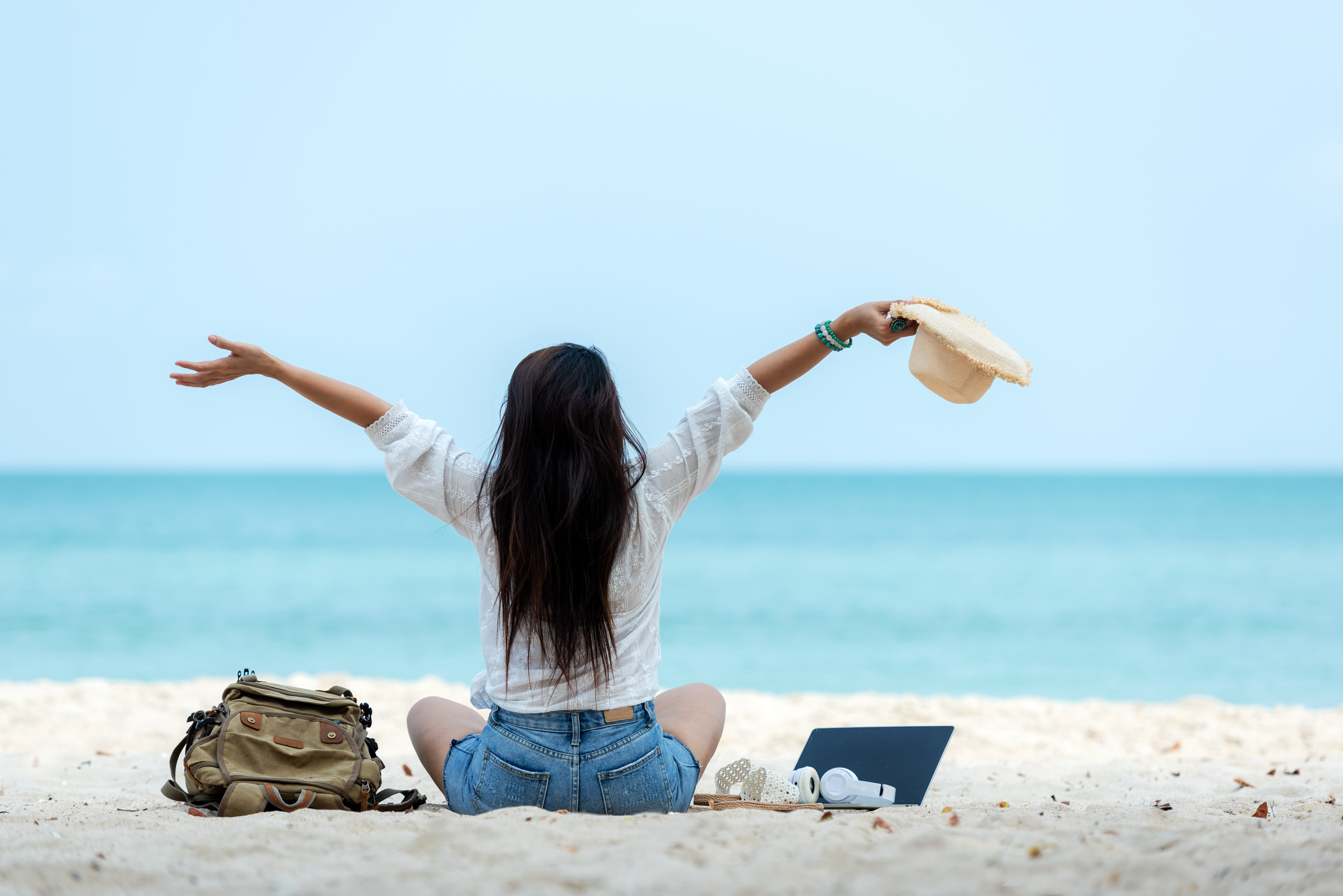 Lifestyle freelance woman raise arms relax after using laptop wo eine Frau sitzt im Schneidersitz am Strand und breitet die Arme nach oben aus