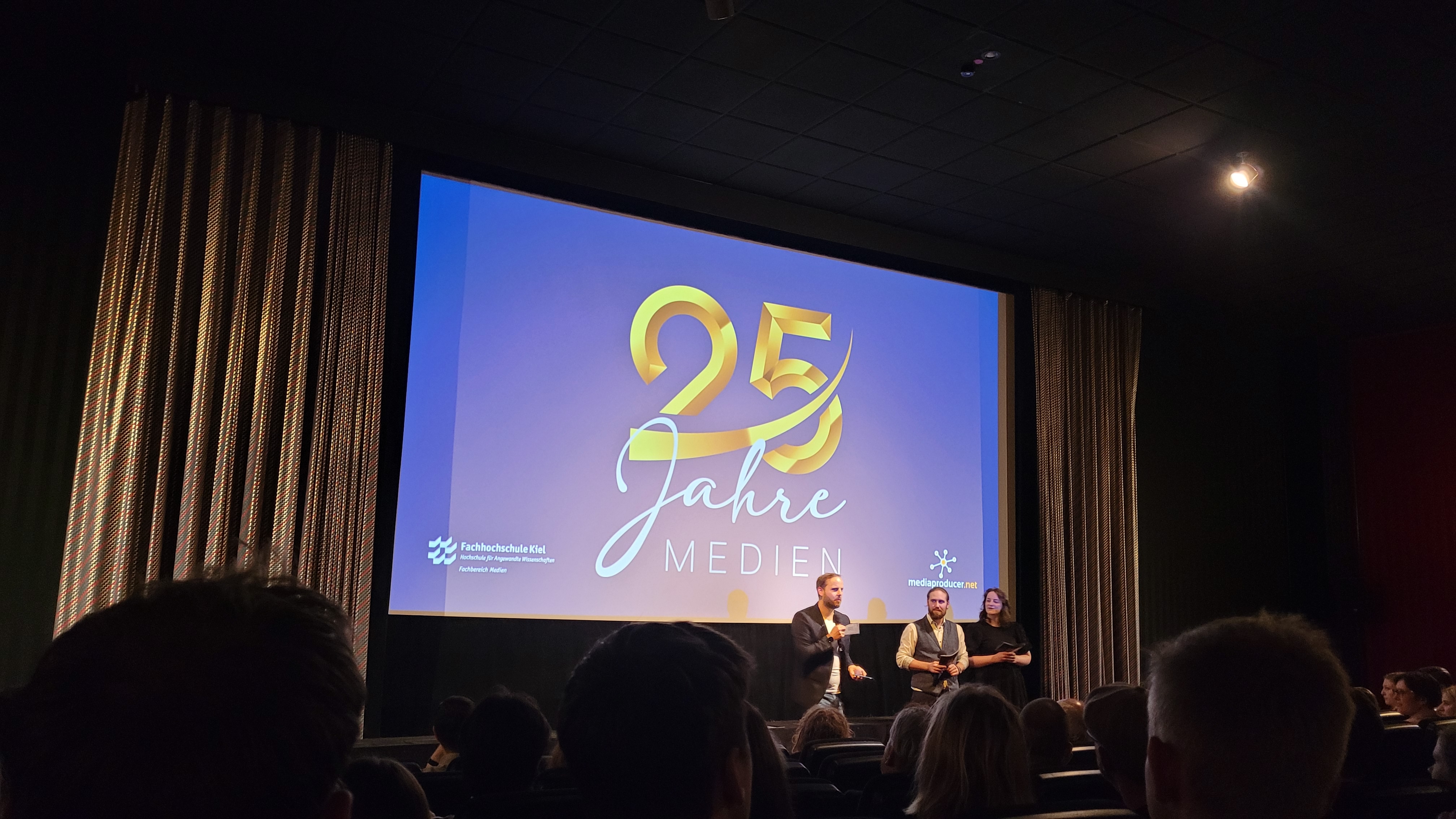 drei Personen stehen vor einer Kino-Leinwand