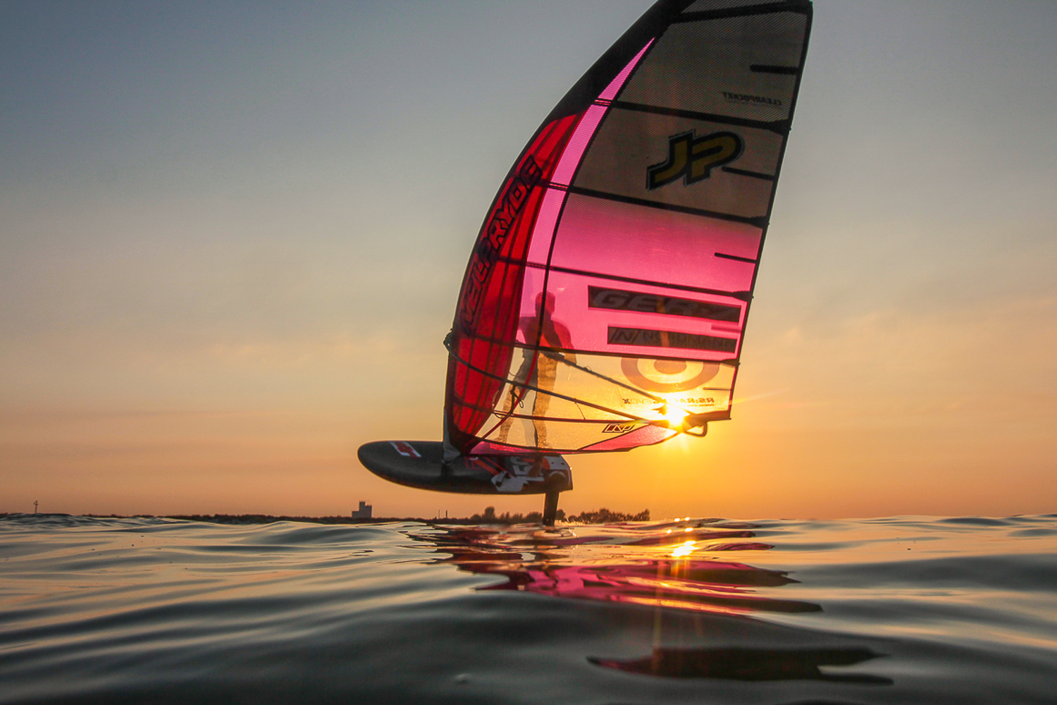 Ein über der Wasseroberfläche schwebender Windsurfer, gleitet durch die untergehende Sonne.