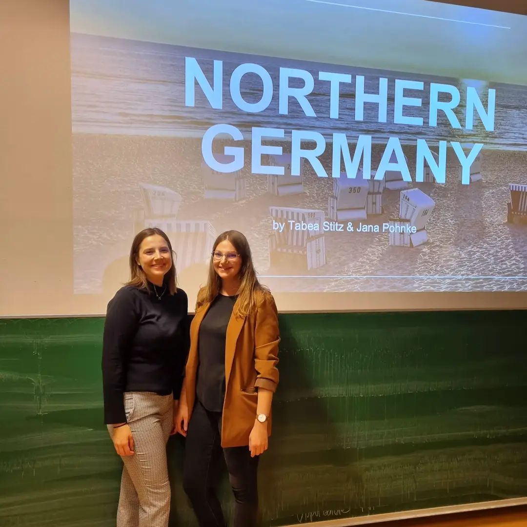 Jana und ihre Kommilitonin Tabea sind vor einer LEinwand zu sehen. Dort zeigt ein Beamer ihre Präsentation über Norddeutschland an, die sie in einem Modul am Joanneum vorgestellt haben.